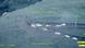 Imagem feita por drone de veículos brancos e algumas pessoas em uma colina