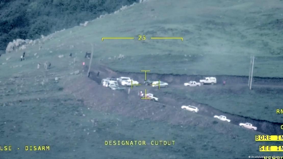 Imagem feita por drone de veículos brancos e algumas pessoas em uma colina