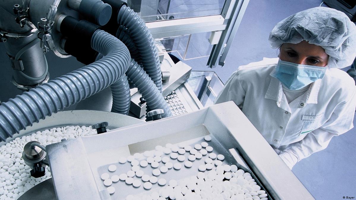 A person in protective clothing looks at pills moving along a belt and through a machine