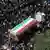 Gran cantidad de gente rodea un cortejo, con un carro cubierto con la bandera iraní.