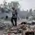 A man in the foreground walks through rubble and clothing strewn in the streets of central Gaza, as children and another man, who is raking, can be seen behind