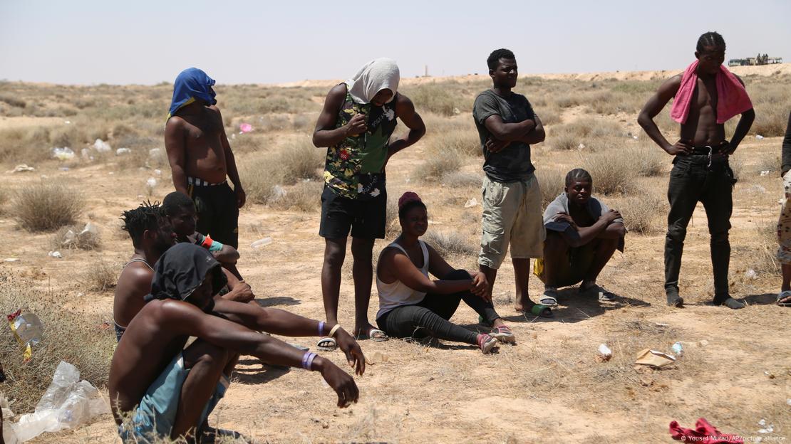 African migrants stand and sit in the desert 