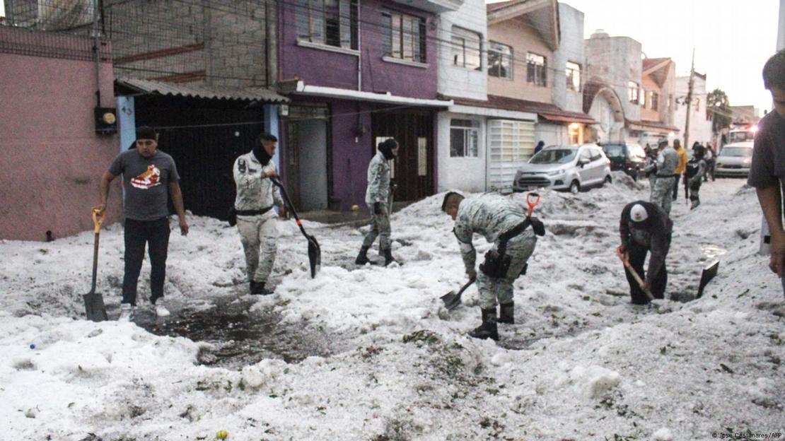 Varios soldados de uniforme, junto a otros civiles, retiran el hielo con palas de una calle.