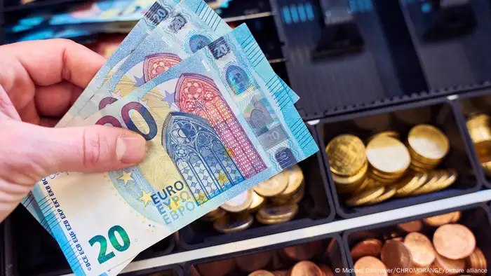 Hand hält mehrere 20 Euro Bargeld, Geldscheine vor die Kasse in einem Geschäft