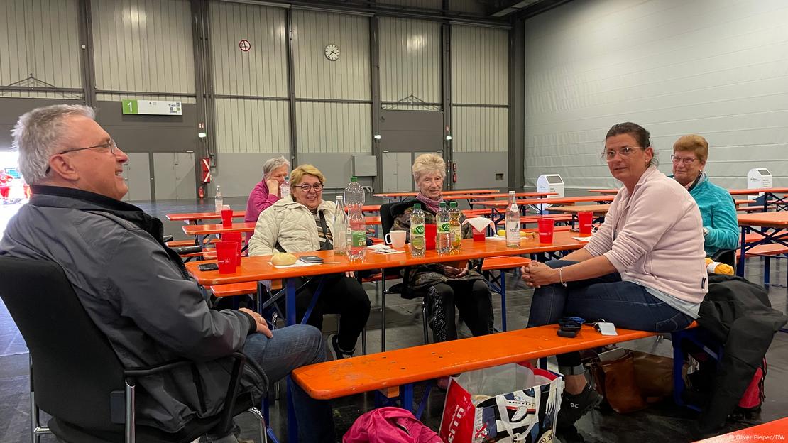 Menschen sitzen auf Holzbänken um einen Tisch herum