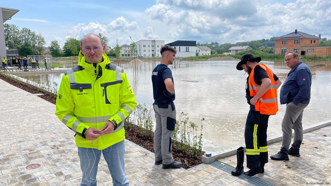 Mann mit gelber Jacke blickt in die Kamera, im Hintergrund weitere drei Männer vor Hochwasser