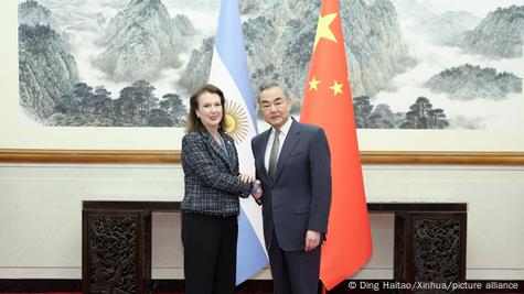 Ministrja e Jashtme e Argjentinës Diana Mondino dhe homologu i saj kinez Wang Yi duke shtrënguar duart në sfond flamujt e dy vendeve