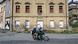Um imóvel com janelas vedadas e, em frente a ele, dois jovens montados em uma moto Um imóvel com janelas vedadas e, em frente a ele, dois jovens montados em uma moto