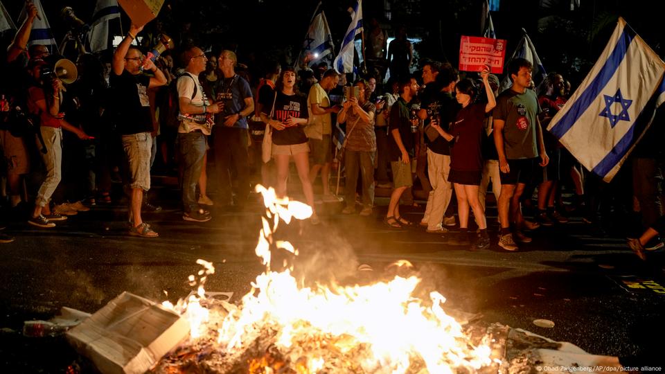 Protesters stand, many holding signs or flags, near a small fire on a street in central Jerusalem. June 17, 2024. Protesters stand, many holding signs or flags, near a small fire on a street in central Jerusalem. June 17, 2024.
