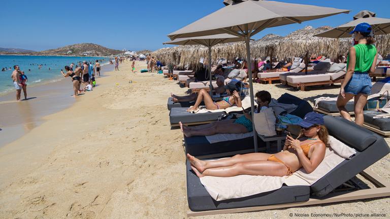 People on a beach on the Greek island of Naxos: Some are lying on sun loungers under parasols, others are swimming in the sea or walking on the sand