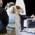 Fila de pessoas. Na frente, mulher deposita voto em urna transparente