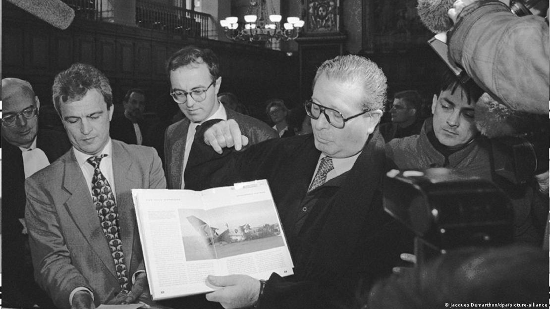 Paul Merlet (C), treasurer of the British Airways passenger association, representing the passengers taken hostage by Iraqi President Saddam Hussein during the Gulf War, points to a photo of their airplane, which was grounded at Kuwait City 02 August 1990