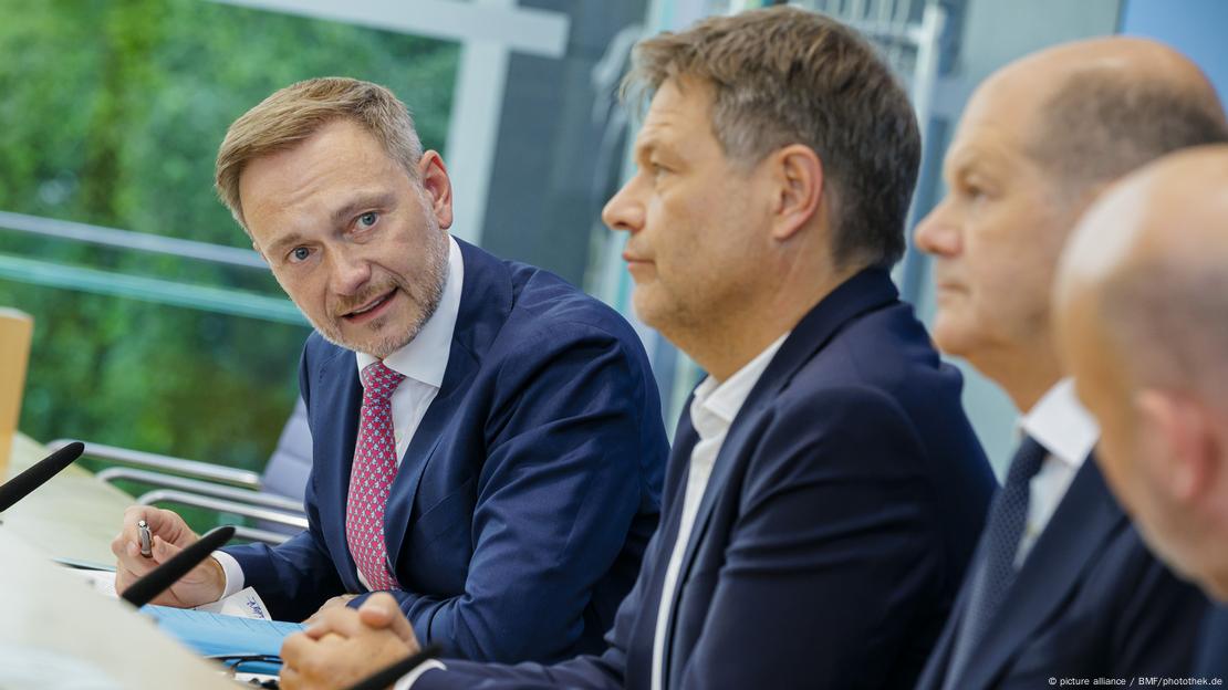 Christian Lindner (FDP), Bundesminister der Finanzen, Olaf Scholz (SPD), Bundeskanzler, und Robert Habeck (Bündnis 90/Die Grünen), Bundesminister für Wirtschaft und Klimaschutz und Vizekanzler, sitzen nebeneinander. Lindner schaut die anderen, die mit ernstem Gesicht nach vorne blicken, auffordernd an.