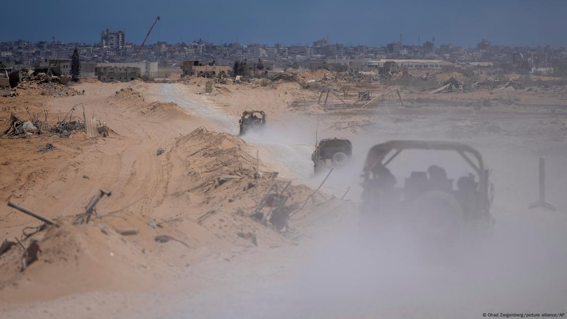 Tres vehículos militares avanzan por un polvoriento camino hacia la ciudad de Rafah, que se atisba al fondo.