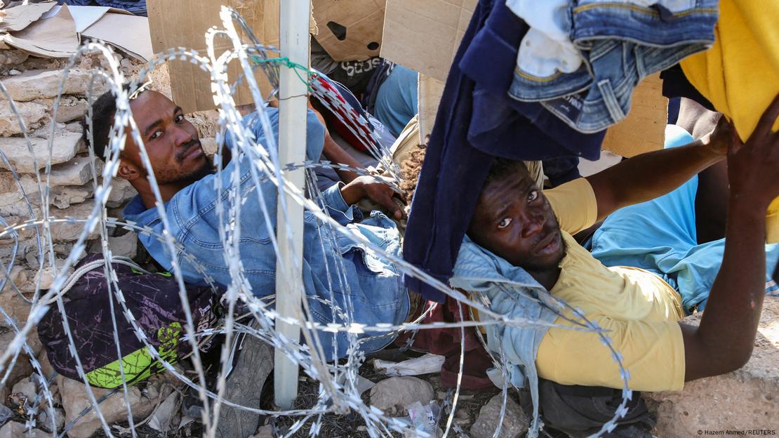 Migrants from Africa are on the floor with their belongings next to them with barbed wire near their heads