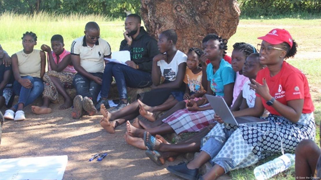 Grupo de jovens africanos sentados à sombra de uma árvore