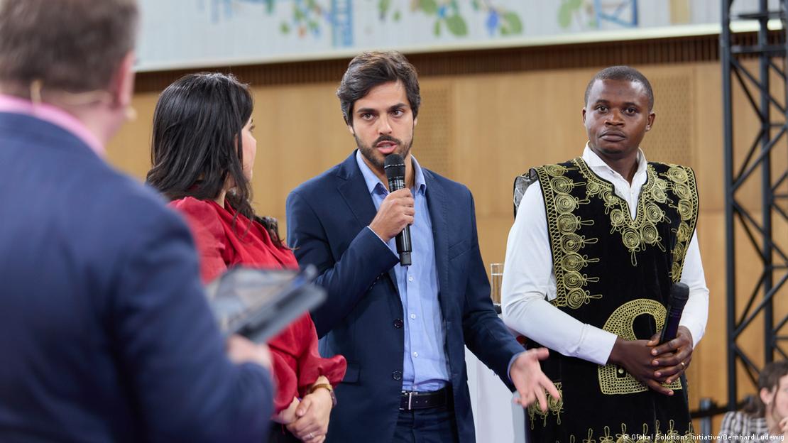 João Tavares fala segurando microfone entre duas pessoas