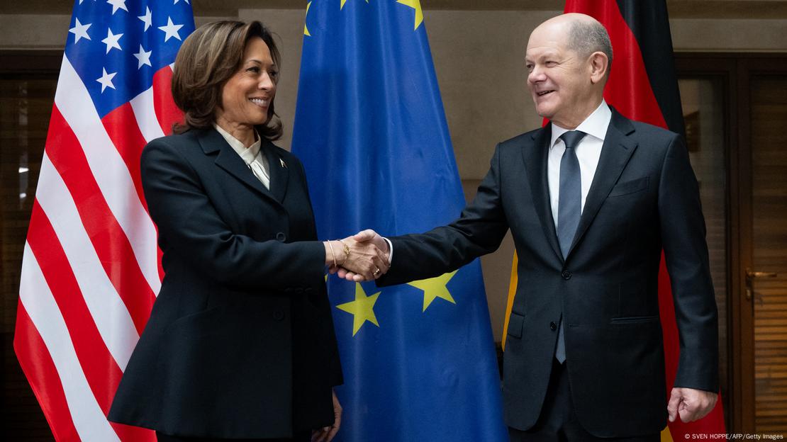 US-Vizepräsidentin Kamala Harris und Bundeskanzler Olaf Scholz reichen sich in München auf der Sicherheitskonferenz im Februar 2024 die Hand vor deutschen, europäischen und amerikanischen Fahnen