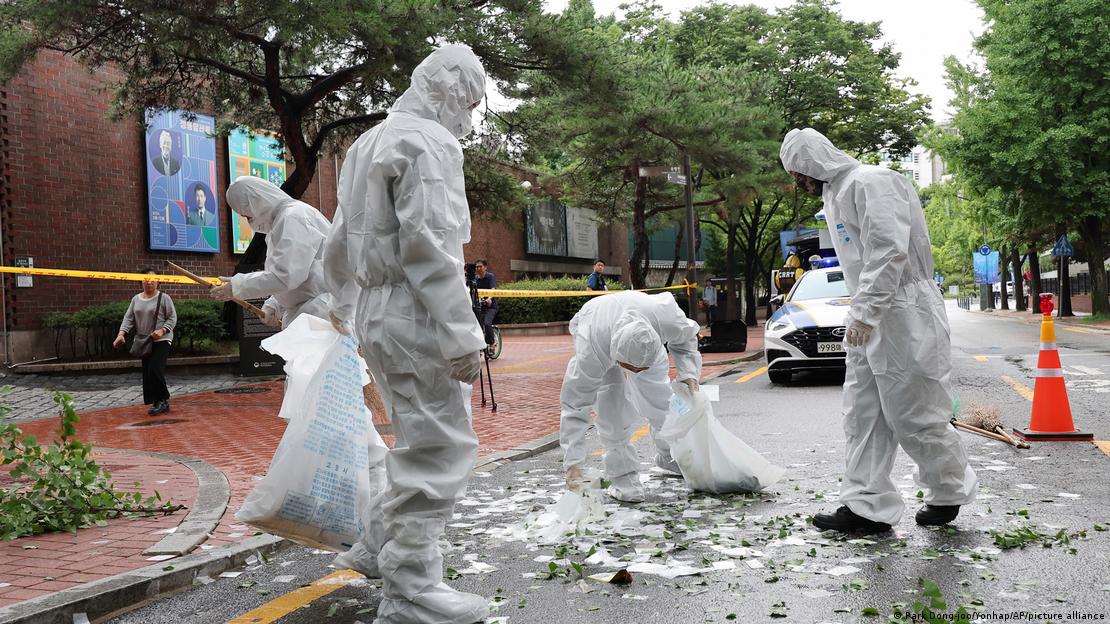 Männer in Schutzanzügen räumen Abfall von einer Straße Männer in Schutzanzügen räumen Abfall von einer Straße