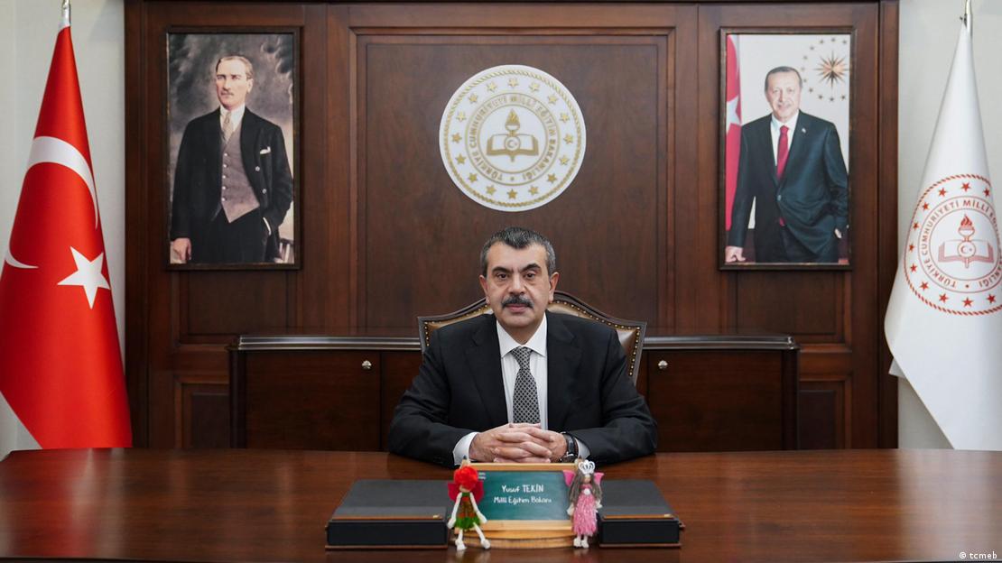 Milli Eğitim Bakanı Yusuf Tekin, arkasında Atatürk ve Erdoğan resimleri ile Türk bayrağının bulunduğu makamında oturuyor.
