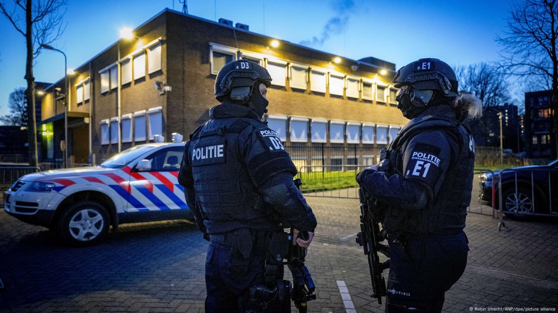 Hollanda'da bir bina önünde bekleyen silahlı iki polis ve bir polis aracı