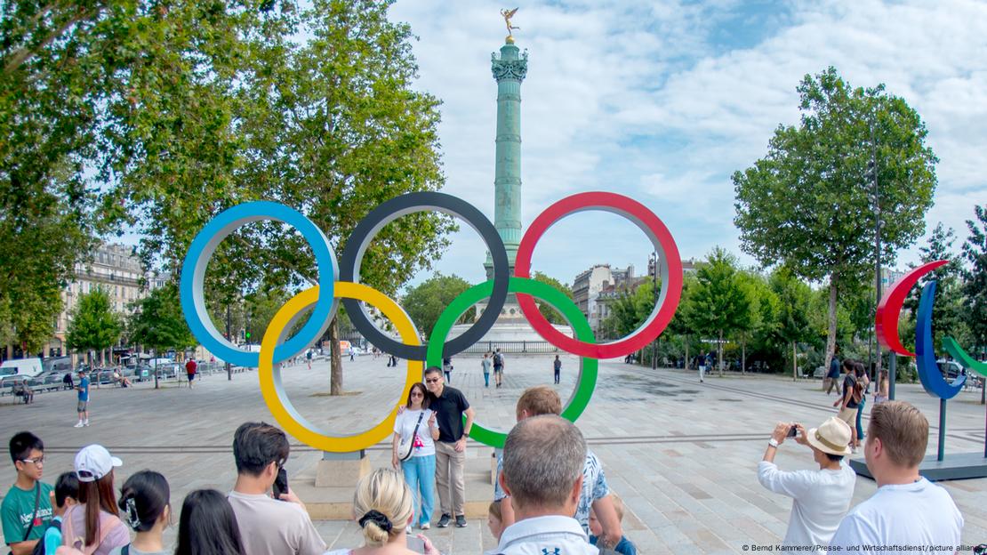 Turistas fotografam anéis olímpicos dos Jogos de Paris 2024 na Bastilha