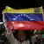 Una mujer sostiene la bandera de Venezuela y mira a cámara.