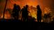 The dark silhouettes of firefighters wearing breathing masks illuminated by a massive forest fire The dark silhouettes of firefighters wearing breathing masks illuminated by a massive forest fire