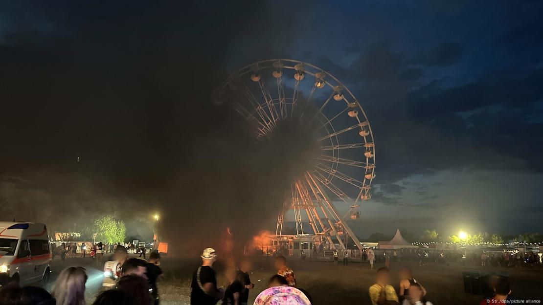 People look at smoke and ferris wheel on fire