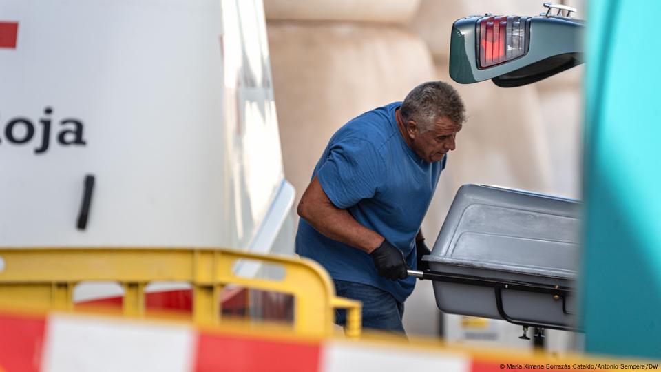 A coroner stows a coffin inside a van.