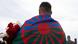 A Roma man seen standing from behind holding red and white flowers, the Roma flag draped over his shoulders A Roma man seen standing from behind holding red and white flowers, the Roma flag draped over his shoulders
