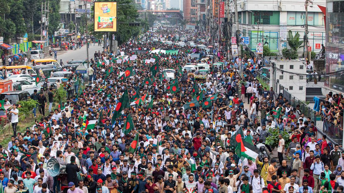 A massive crowd of people march in protest, many waving Bangladeshi and Palestinian flags, in the streets of Dhakar, Bangladesh