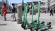 Four green e-scooters in central street of Madrid; pedestrians are seen in the background Four green e-scooters in central street of Madrid; pedestrians are seen in the background