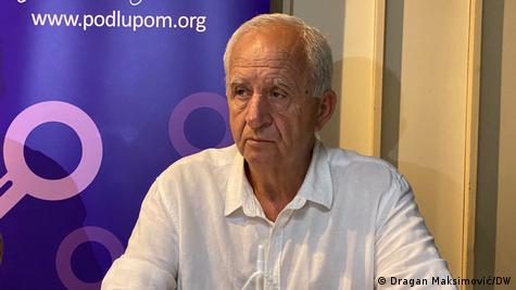 Sredovječan muškarac a iza njega logo NGO-a "Pod lupom" Sredovječan muškarac a iza njega logo NGO-a "Pod lupom"