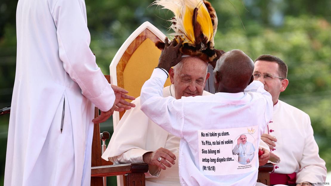 Eine Person setzt Papst Franziskus eine Kopfbedeckung auf