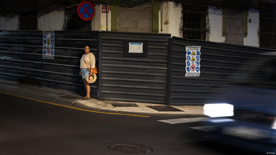 Kamila em uma esquina de rua movimentada, onde tapumes escondem uma casa em construção 