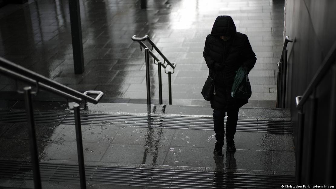 Bu fotoğrafta biri kişi yağmurlu havada elinde şemsiye ile sokaktaki merdivenleri çıkıyor