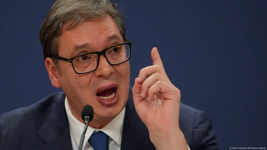 President Aleksandar Vucic wears glasses and speaks into a microphone, finger raised