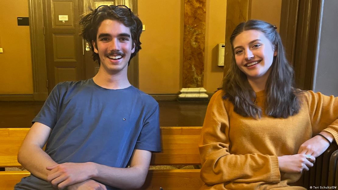 Mlađi muškarac i žena sjede na klupi u učionici i smiju se u kameru