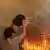 A woman with a bucket full of water on a balcony trying to extinguish flames