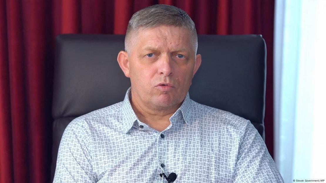 Slovakian Prime Minister Robert Fico sits on a high leather chair and speaks in a microphone attached to the button placket of his shirt