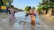 Schoolboys wade through a flooded street, one of them pushes a bicycle