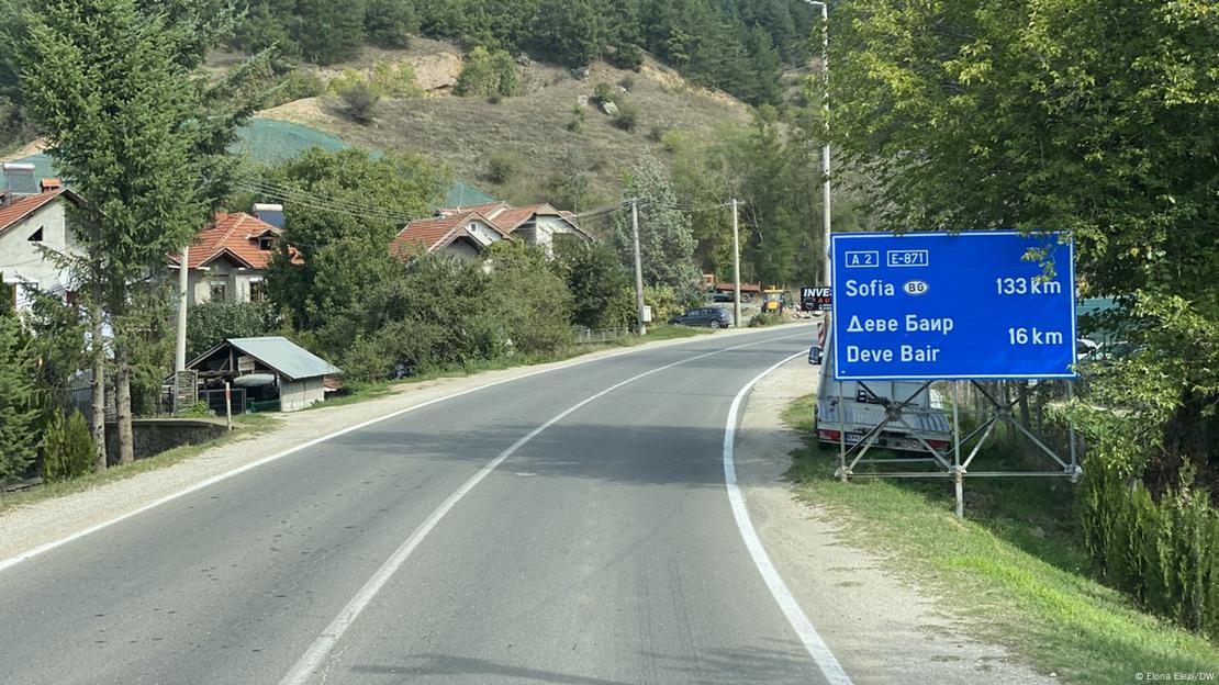 Korridori 8 në kufirin mes Maqedonisë së Veriut dhe Bullgarisë, rruga e asfaltuar, tabela qarkullimi, Sofja 133 km larg, në sfond shtëpi dhe pemë