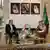 Two men sitting on chairs and the Iranian and Saudi flags