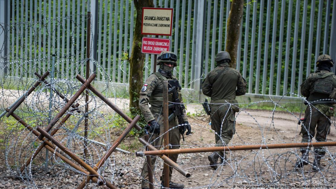 Drei Soldaten hinter Stacheldrahtzaun an der Grenze zu Belarus