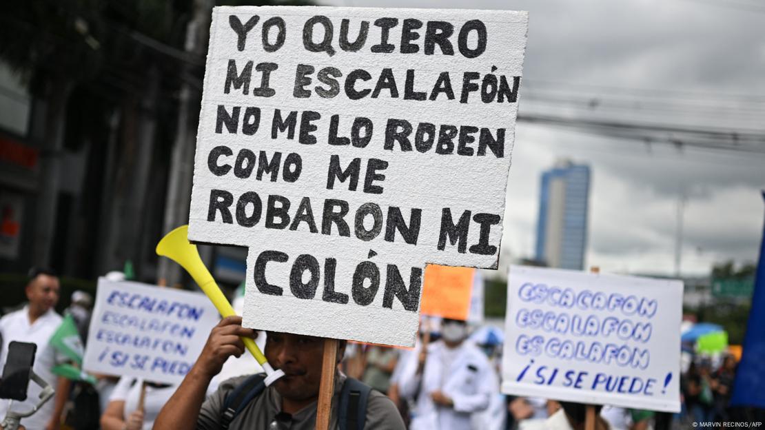 Foto de una persona que sostiene un cartel que dice "yo quiero mi escalafón, no me lo roben como me robaron mi colón".