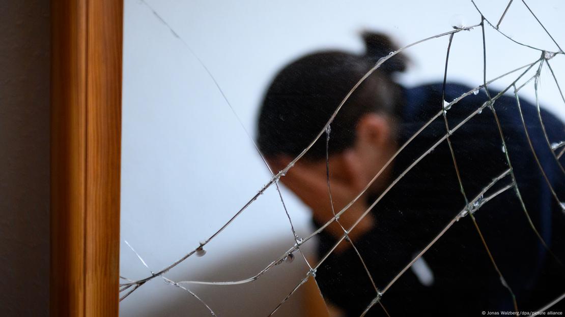Πίσω από ένα σπασμένο τζάμι μια γυναίκα κρύβει το πρόσωπο στα χέρια της Πίσω από ένα σπασμένο τζάμι μια γυναίκα κρύβει το πρόσωπο στα χέρια της