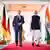 Bundeskanzler Olaf Scholz (links) und der indische Ministerpräsident Narendra Modi in einer Säulenhalle, die links mit deutschen, rechts mit indischen Flaggen dekoriert ist