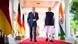 Scholz y Modi caminan por un alfombra roja, flanqueados por banderas de India y Alemania. Scholz y Modi caminan por un alfombra roja, flanqueados por banderas de India y Alemania.