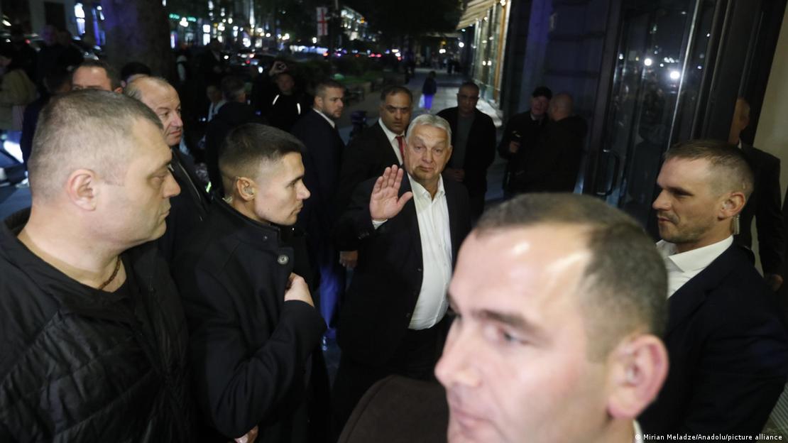 Viktor Orbán acena para a câmera, rodeado de seguranças Viktor Orbán acena para a câmera, rodeado de seguranças